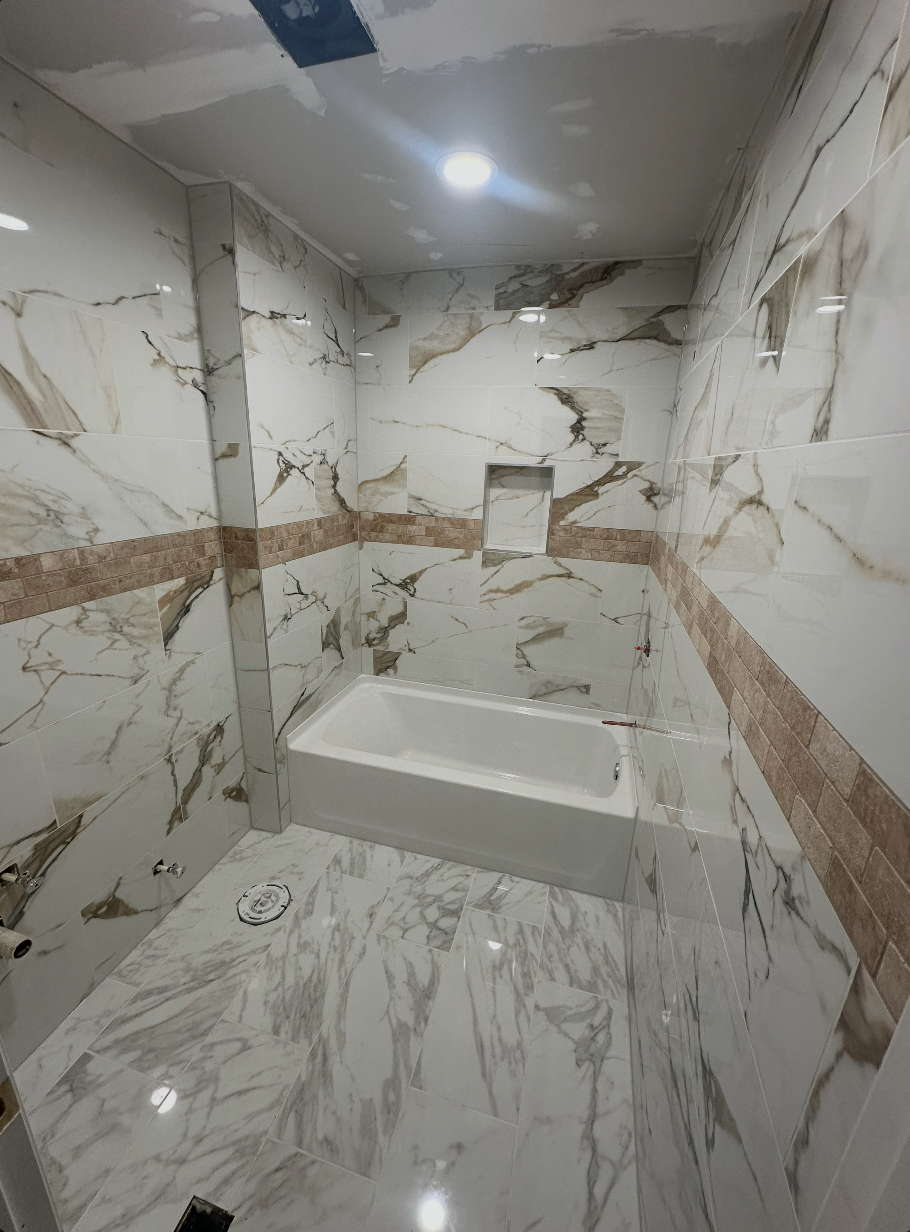 Tub surround with glossy marble-look wall tile, stone-colored accent band, and recessed niche
