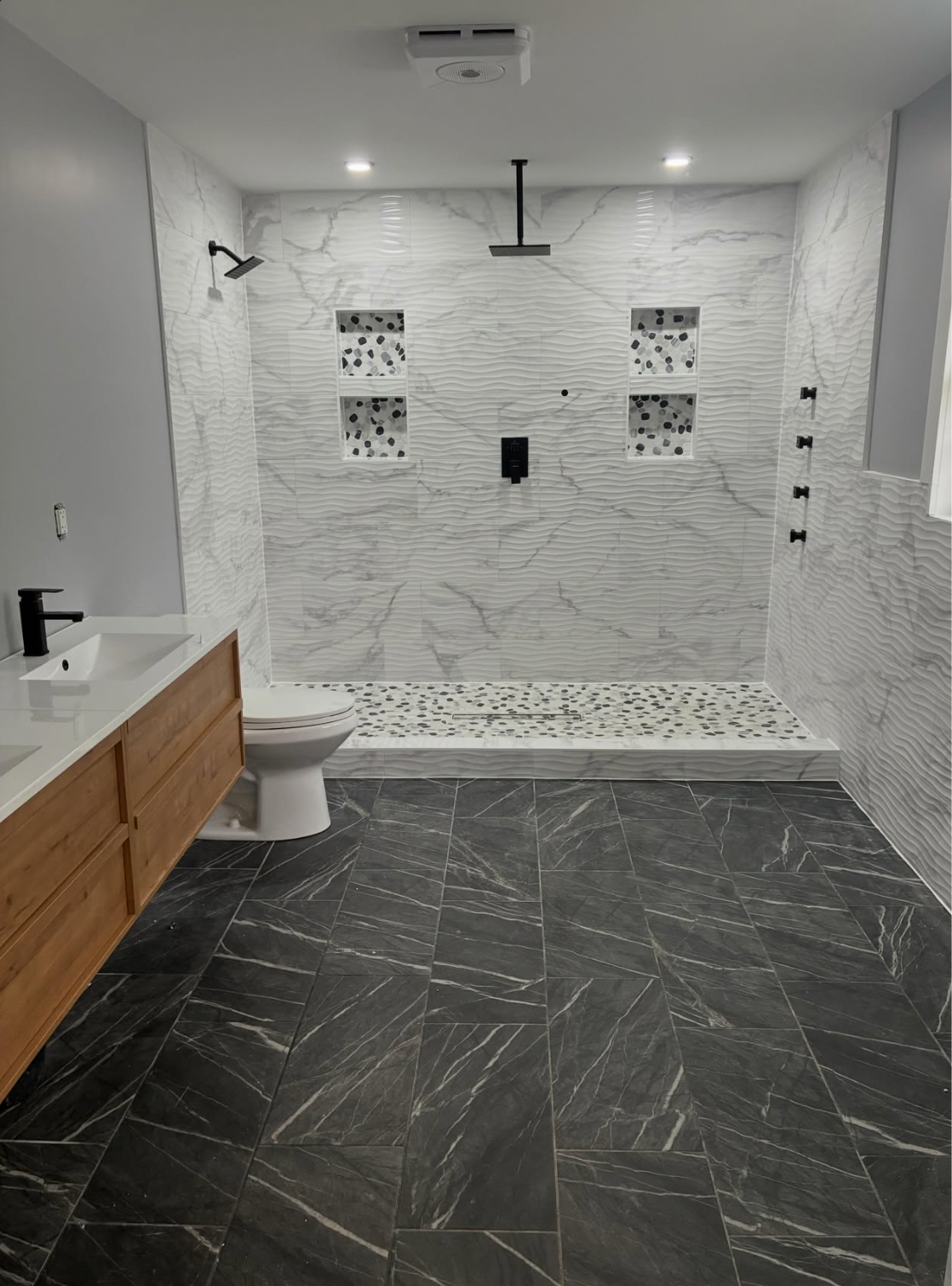 Primary bathroom with a large walk-in shower, textured white tile, pebble accents, and dark floor tile