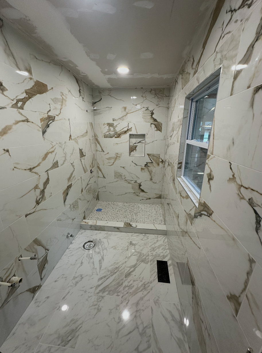 Walk-in shower with large marble-look wall tile, pebble mosaic floor, window trim, and niche
